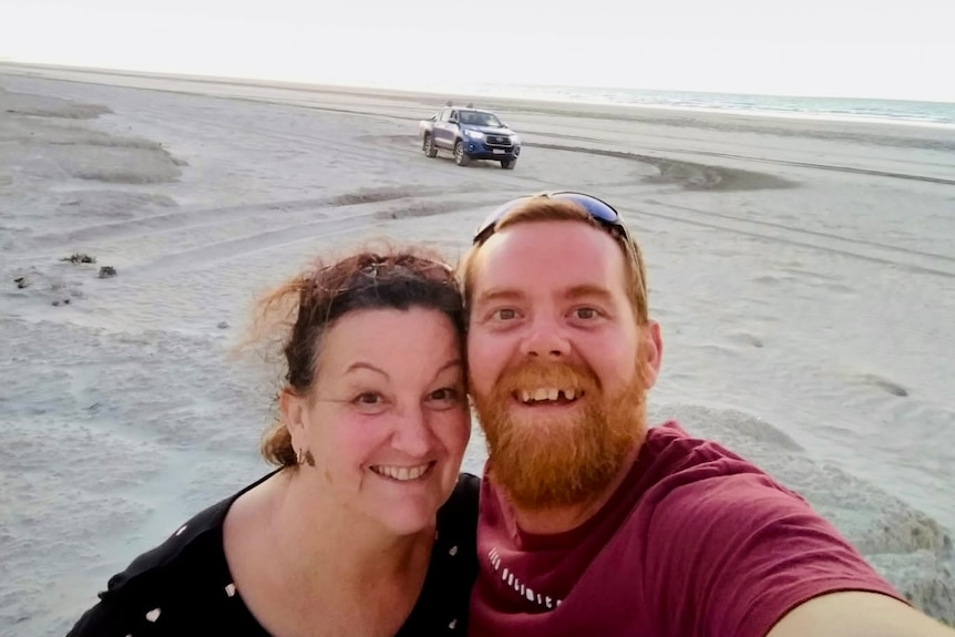 A man and a woman stand smiling at a beach