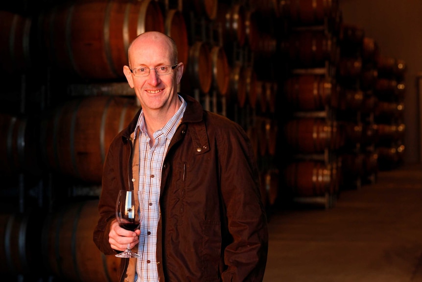 a man in a blazer in a wine cellar holding a glass of wine.