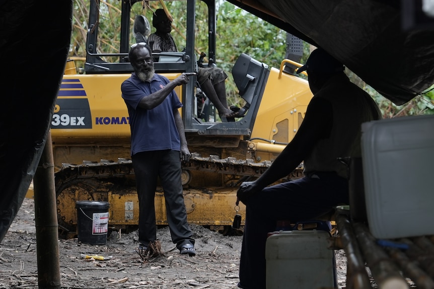 Dennis working with other veterans pointing and pictured next to a tractor.