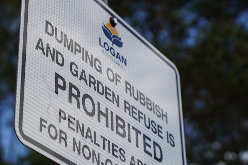 Close up of a white street sign with the City of Logan's emblem printed on it. The text warns against waste dumping.