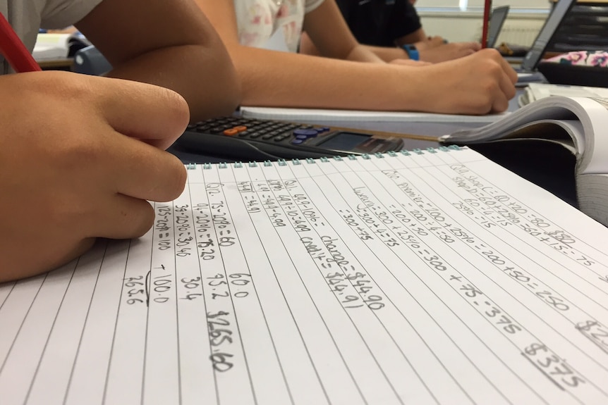 Teenage students solve maths problems in workbooks.