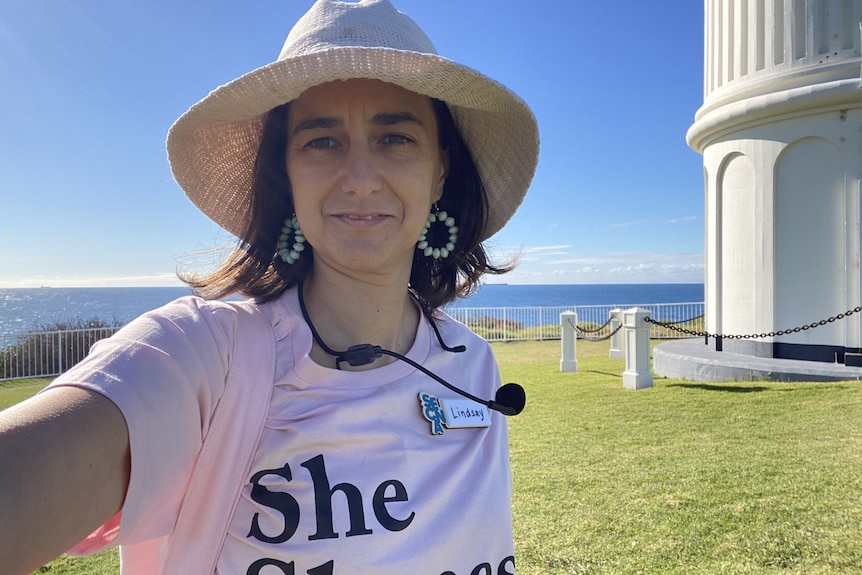 woman in hate and 'she shapes history' T-shirt in front of lighthouse