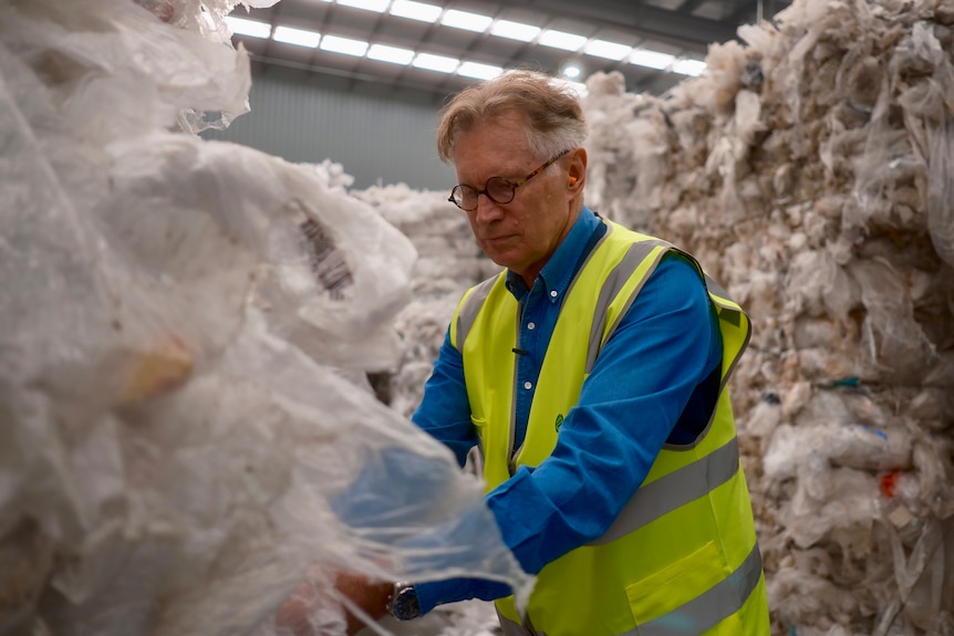 A white haired man in glasses, a blue collared shirt and yellow vest works with a pile of white soft plastic.