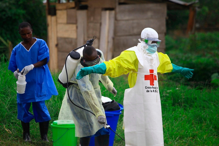 A person in a hazmat suit being washed down by other workers.