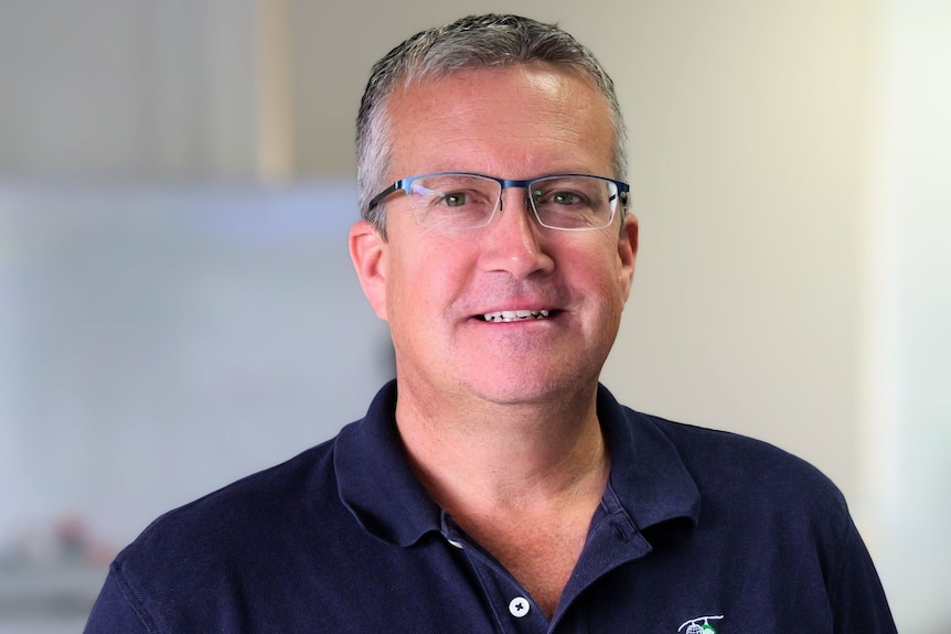 A man in a polo shirt and glasses smiling.