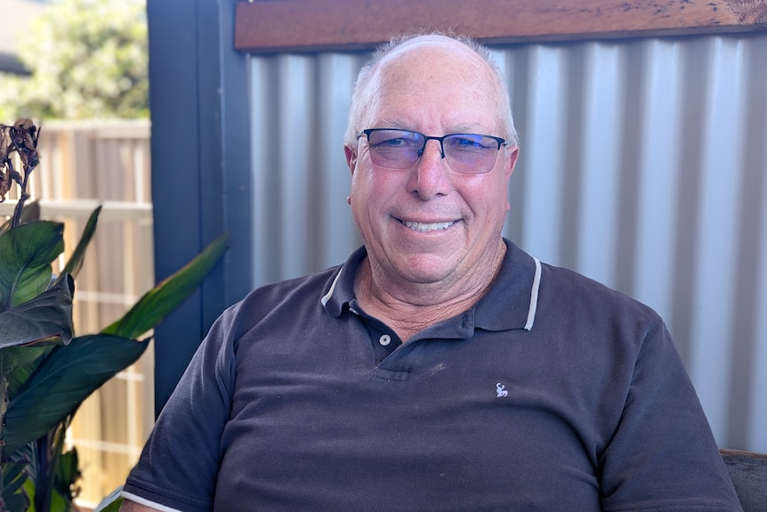 A grey-haired balding fair-skinned bespectacled man, Steve, in grey polo sits.