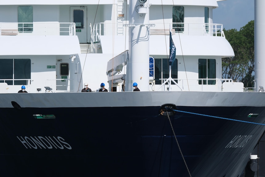 people in hard hats stand on the bow of a ship as it docks