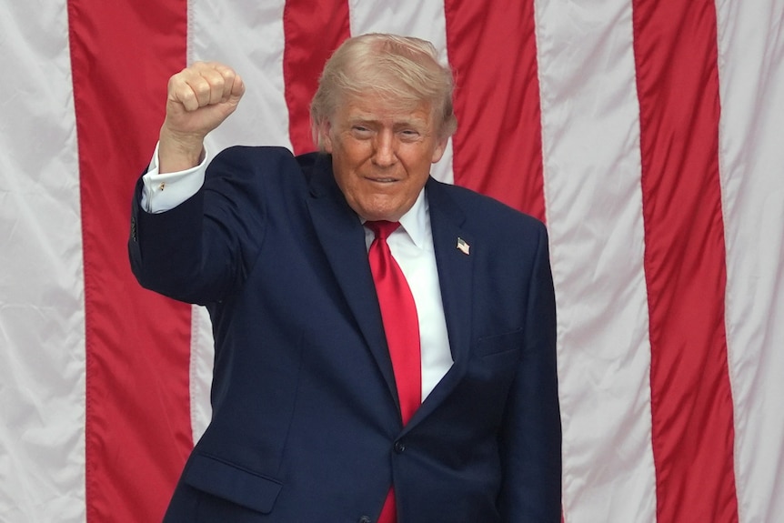 Donald Trump does a fist bump into the air while standing in front of an american flag