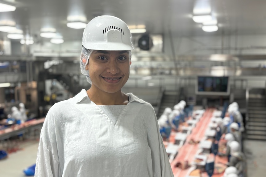 A smiling woman standing above a factory floor.