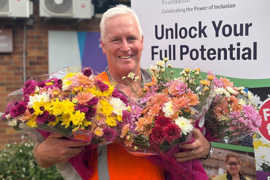 A man in a high-vis vest holding several flower bouquets while smiling