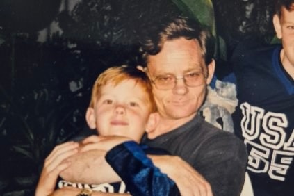A young boy sits smiling on his father's lap.