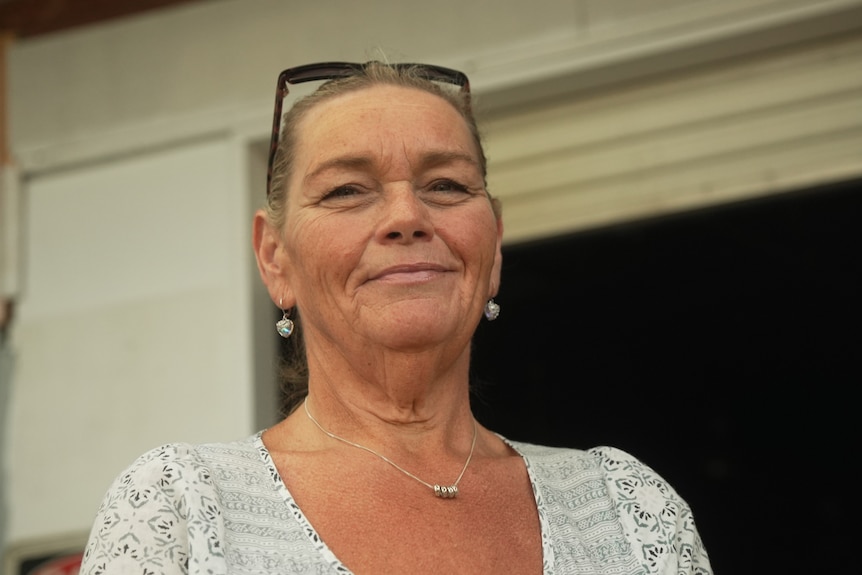 A woman with tanned skin poses for camera. She rests her sunglasses on her head.