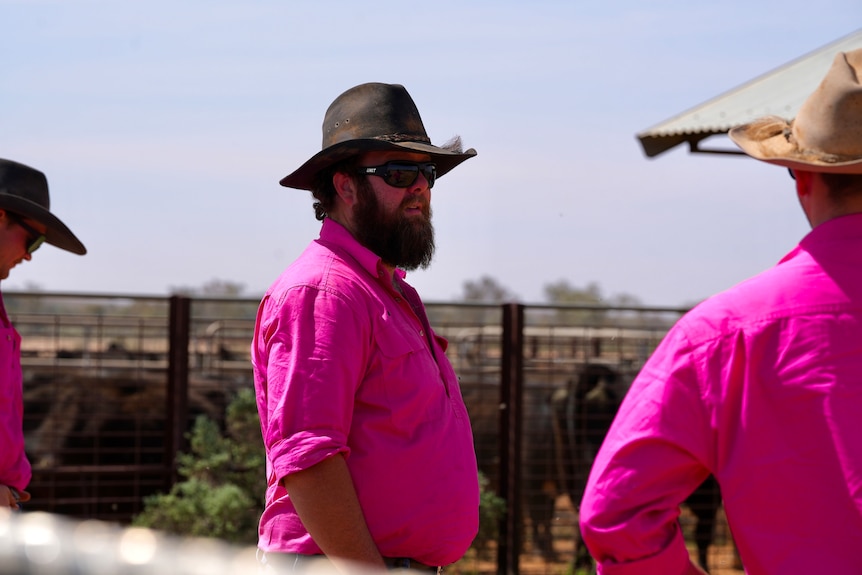 Sam Beven wearing a pink shirt, hat and sunglasses in the cattle yards