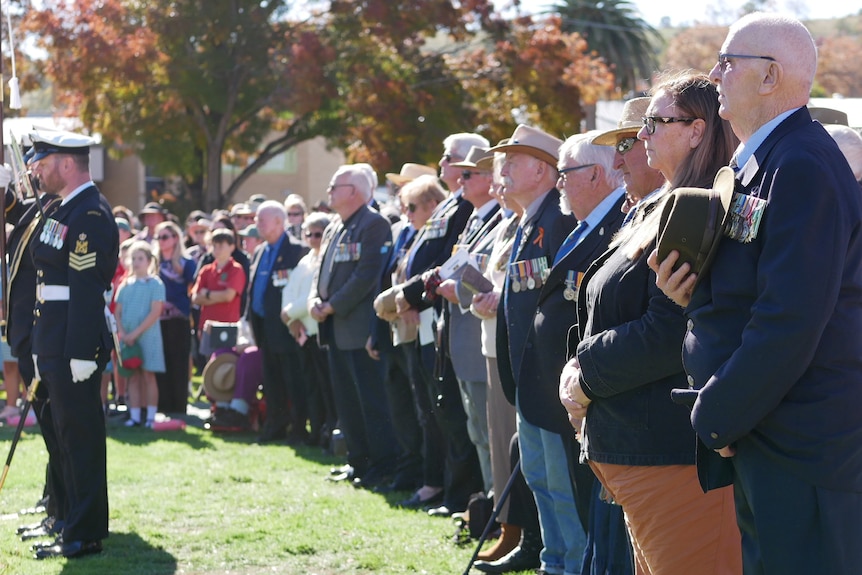 A lineup of apeople dressed formally standing up, with a navy soldier standing in front