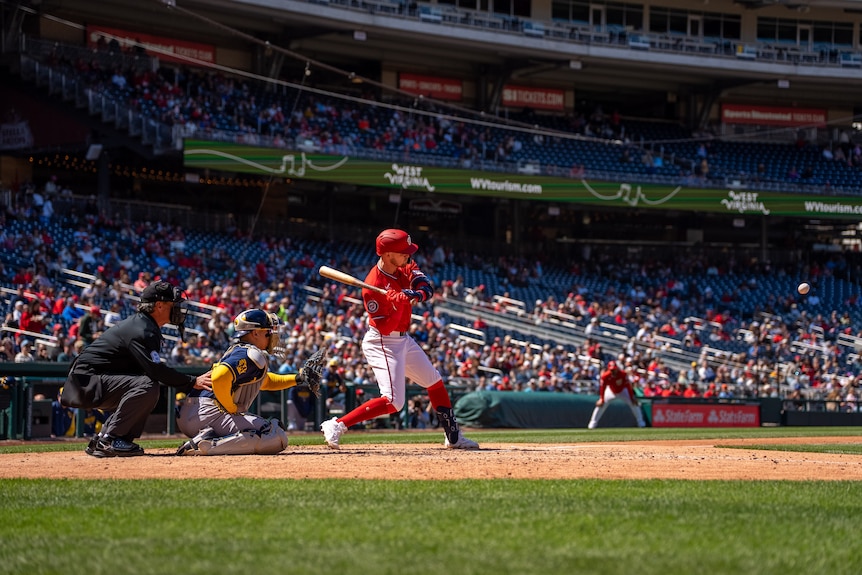 Curtis Mead, wearing red kit, swings for a pitched ball on the field during a baseball game.