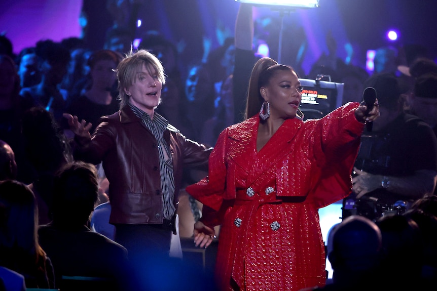 A man stands next to Queen Latifah waving.