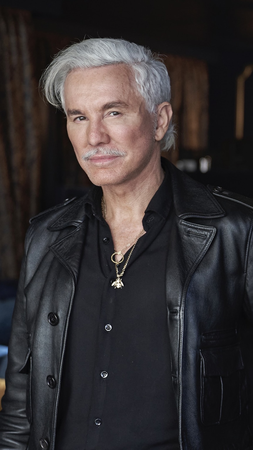 A middle aged caucasian man wearing black and with grey hair looks on with a neutral expression