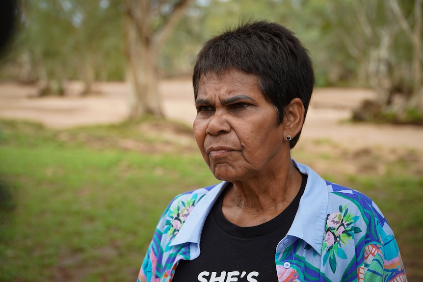A woman with short hair wearing a blue blouse over a black shirt looks to the left