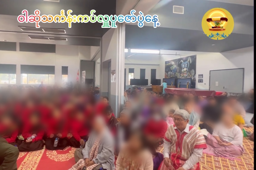 Saw Wah sitting at the front of a crowd of people who have been blurred out.