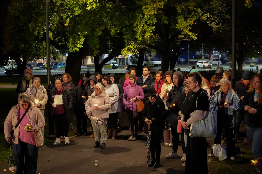 A crowd of dozens holding candles, some wearing pink, at a vigil.