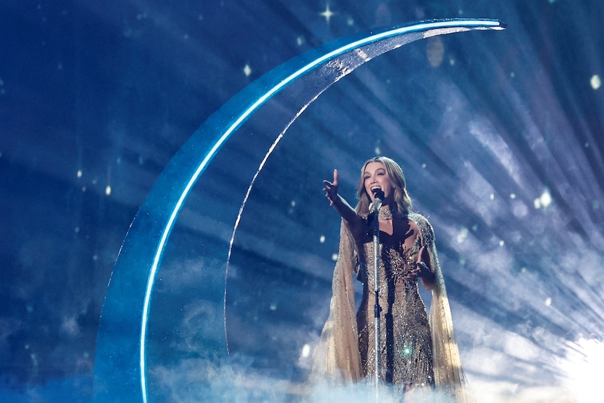 Delta Goodrem sings, arm outstretched, in front of a crescent moon on the Eurovision stage