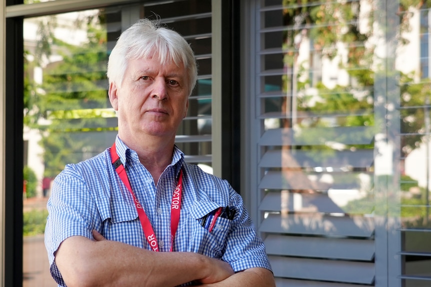 A doctor with his arms folded stands in front of a window.