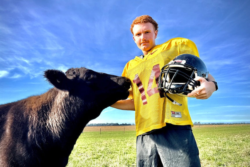 A red headed 19 year-old boy with a football on a farm.