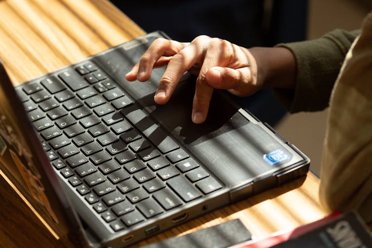 A Black person's hands seen on a laptop keyboard.