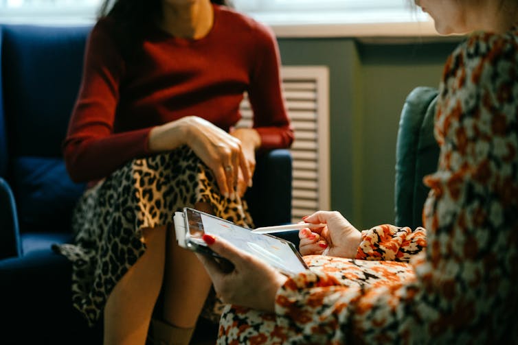 Two people sitting in armchairs facing each other, the person in the foreground holding a stylus and touchpad