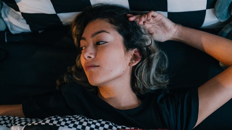 Woman lying in bed, looking out of window with a dismayed look on her face.