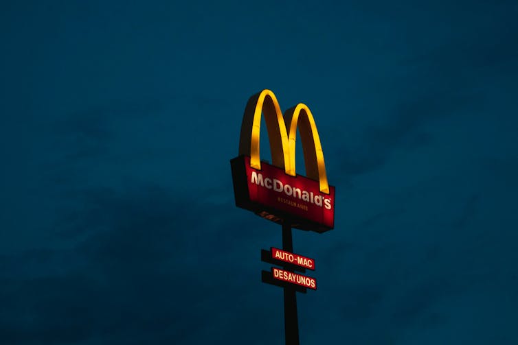 A lit-up McDonalds drive through sign against a night sky.