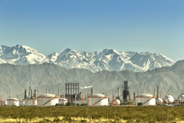 oil refinery in foreground, large snowy mountains behind.