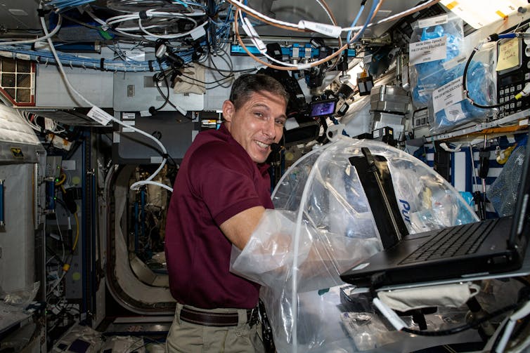A man in a red shirt has his hands in a plastic glovebox in a confined space.