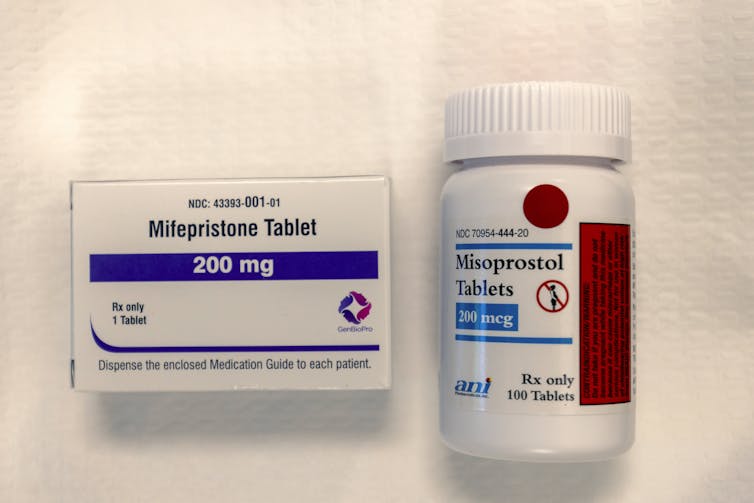 A packet of mifepristone and a pill bottle of misoprostol on a white background