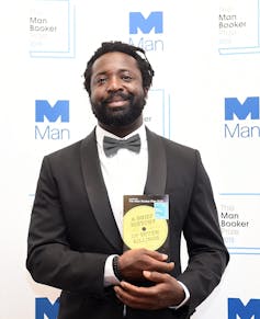 a Black man in a tuxedo holding his book