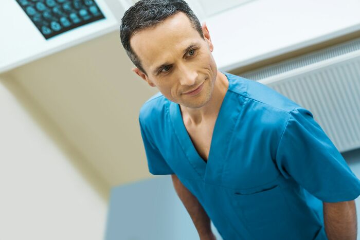Male medical worker in blue scrubs smiling in clinical setting