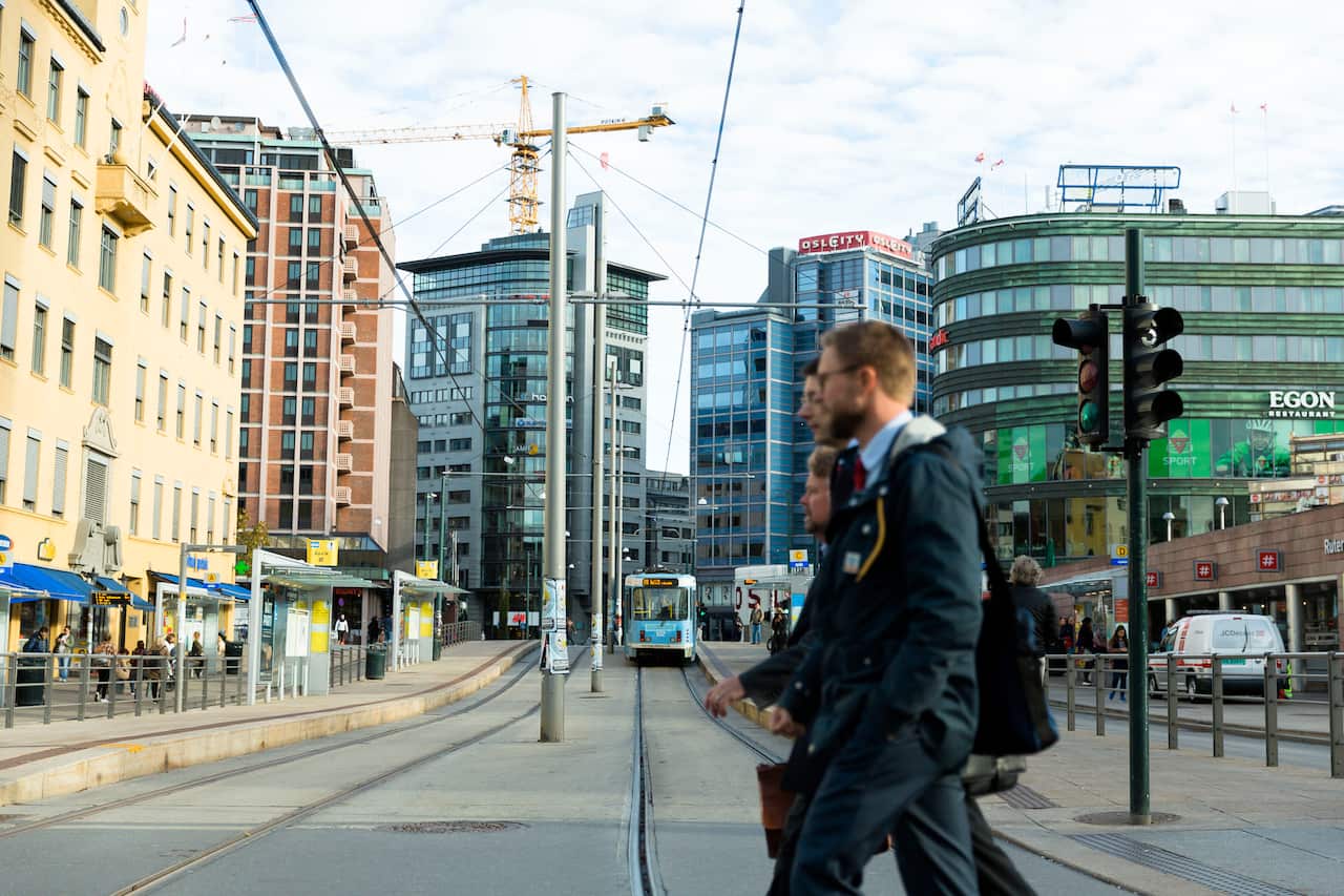 Pedestrians walking past a tram station. There are office buildings in the background