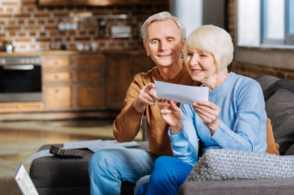 An elderly couple on a sofa reviewing documents, with the man pointing and the woman holding a paper.