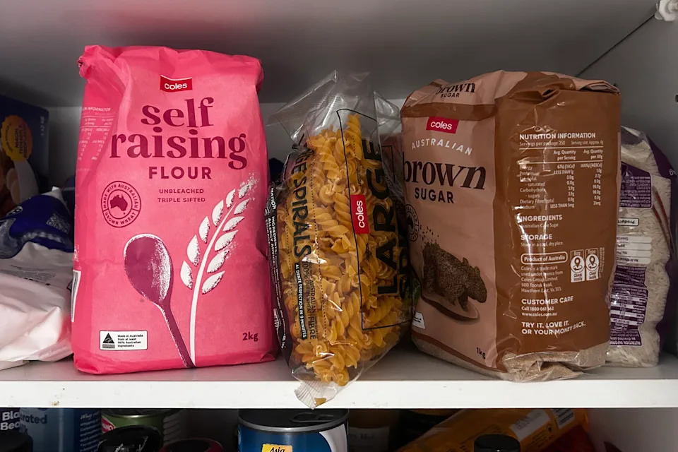 Coles branded flour, pasta and brown sugar sits in a cupboard.