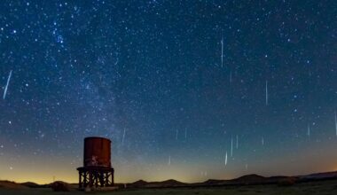 A dark blue night sky is streaked with white meteors moving through space with a rusty cylindrical water tower below.
