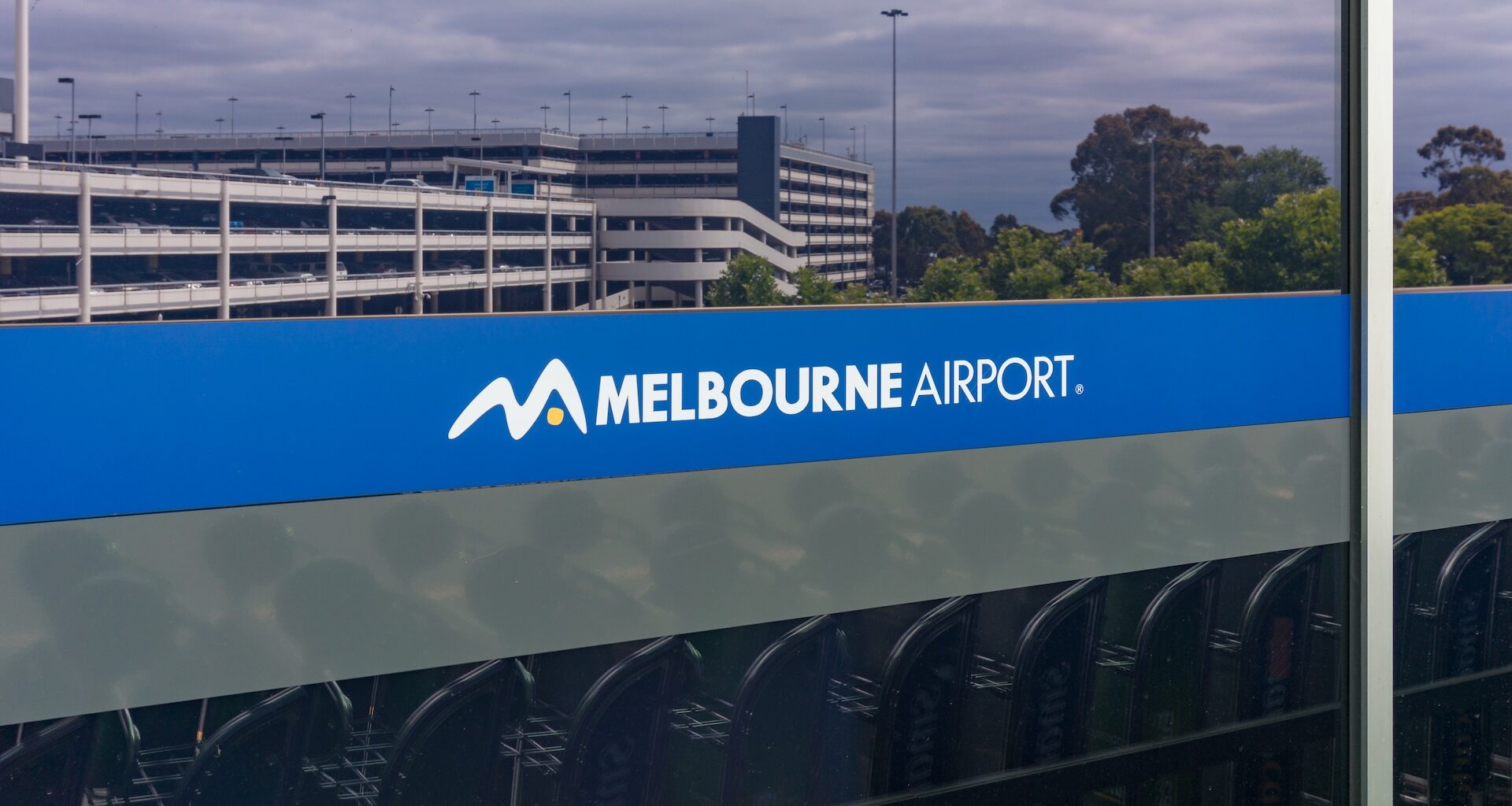A sign displaying the logo and name of Melbourne Airport beside a parking structure.