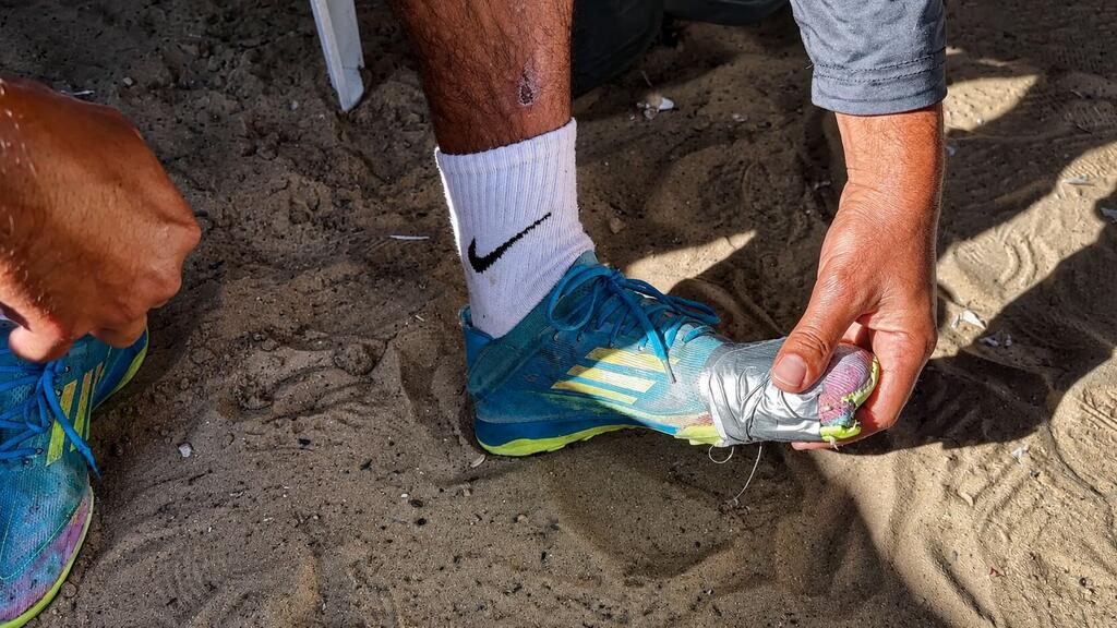A displaced football player from Rafah prepares his cleats in a sand camp in Al-Mawasi, west of Khan Younis, Gaza.