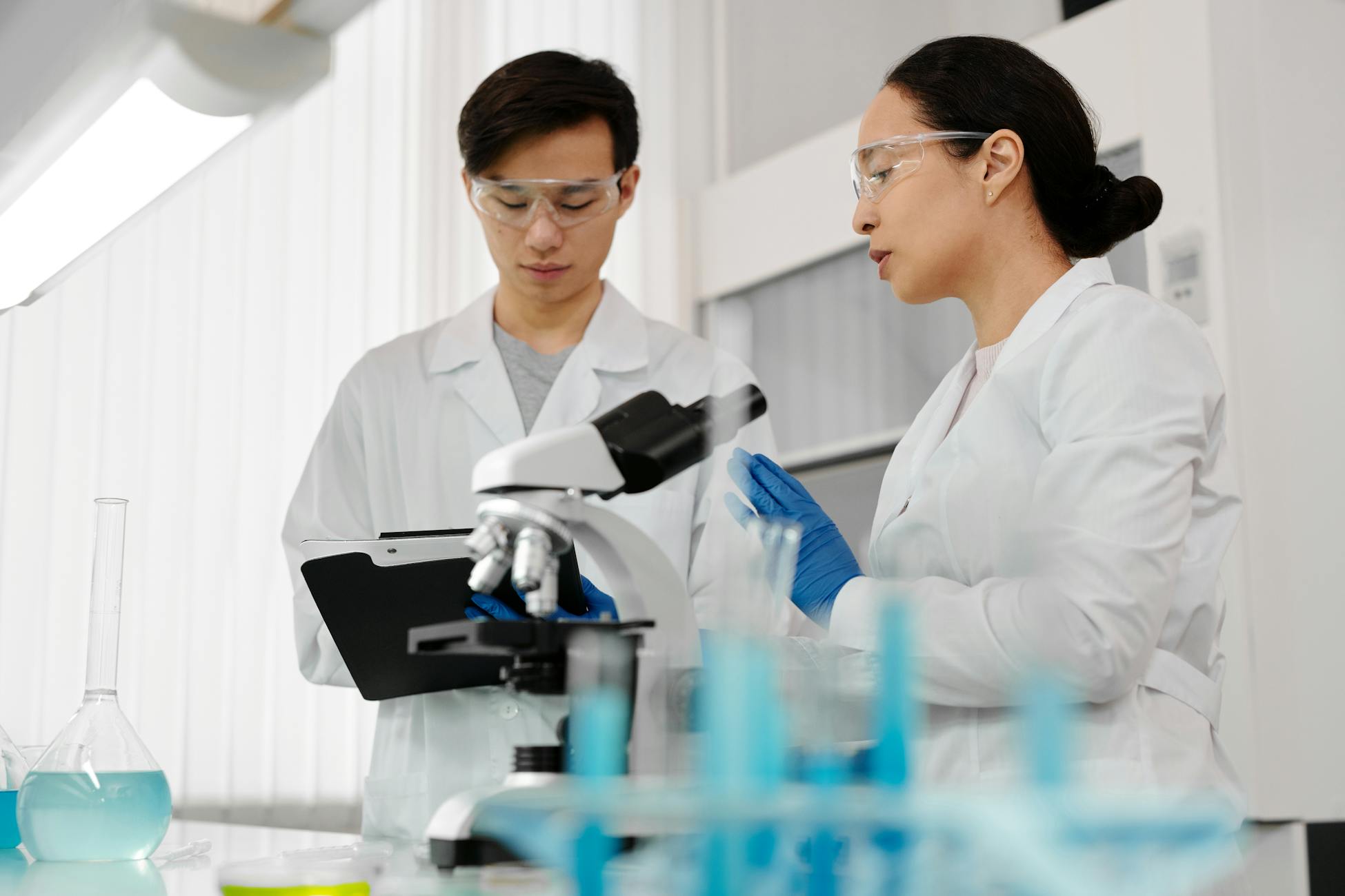 Asian scientists in lab coats discussing research with a microscope in a laboratory setting.