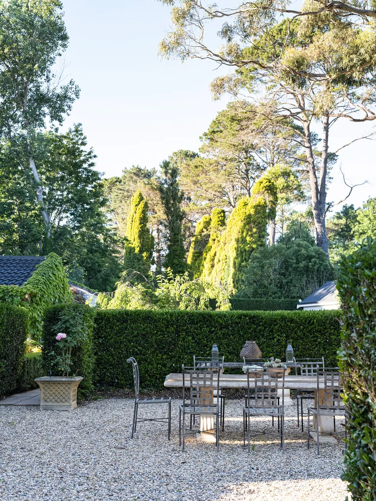A gravel outdoor dining area surrounded by trees and hedges
