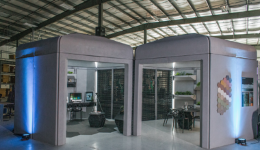 Two boxy structures, one with an office-like interior and the other with an eating area, side-by-side in a hangar-like location
