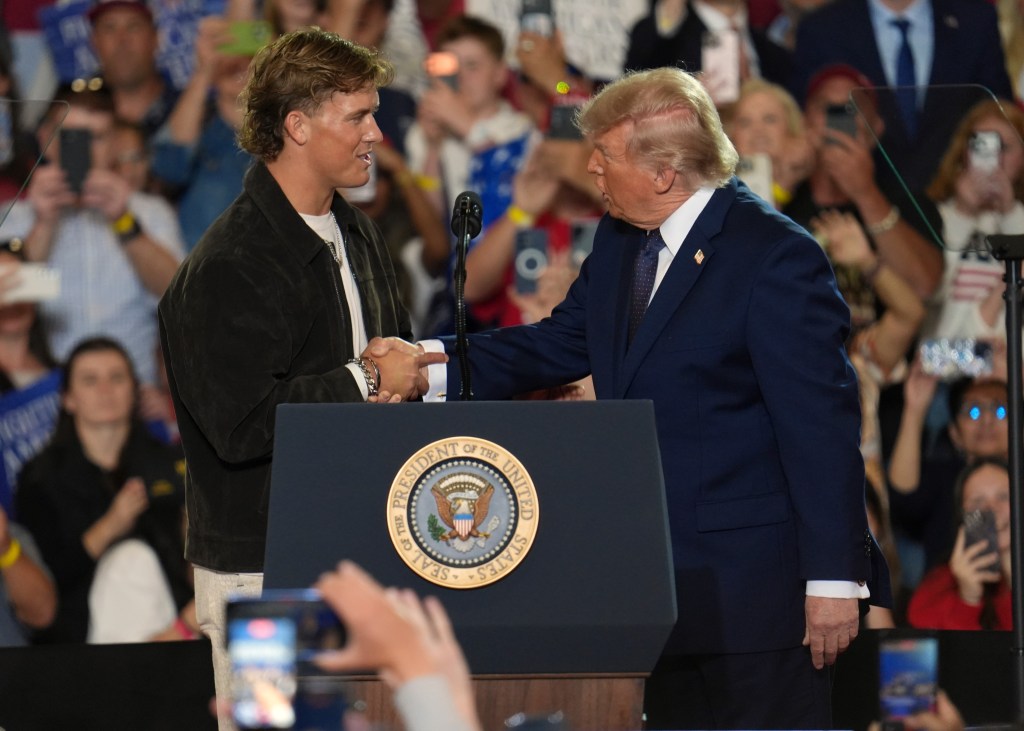 NFL quarterback Jaxson Dart shaking hands with former President Donald Trump at a podium during a Fighting For American Workers event.
