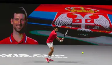 Novak Djokovic playing tennis on indoor court with Serbian flag backdrop