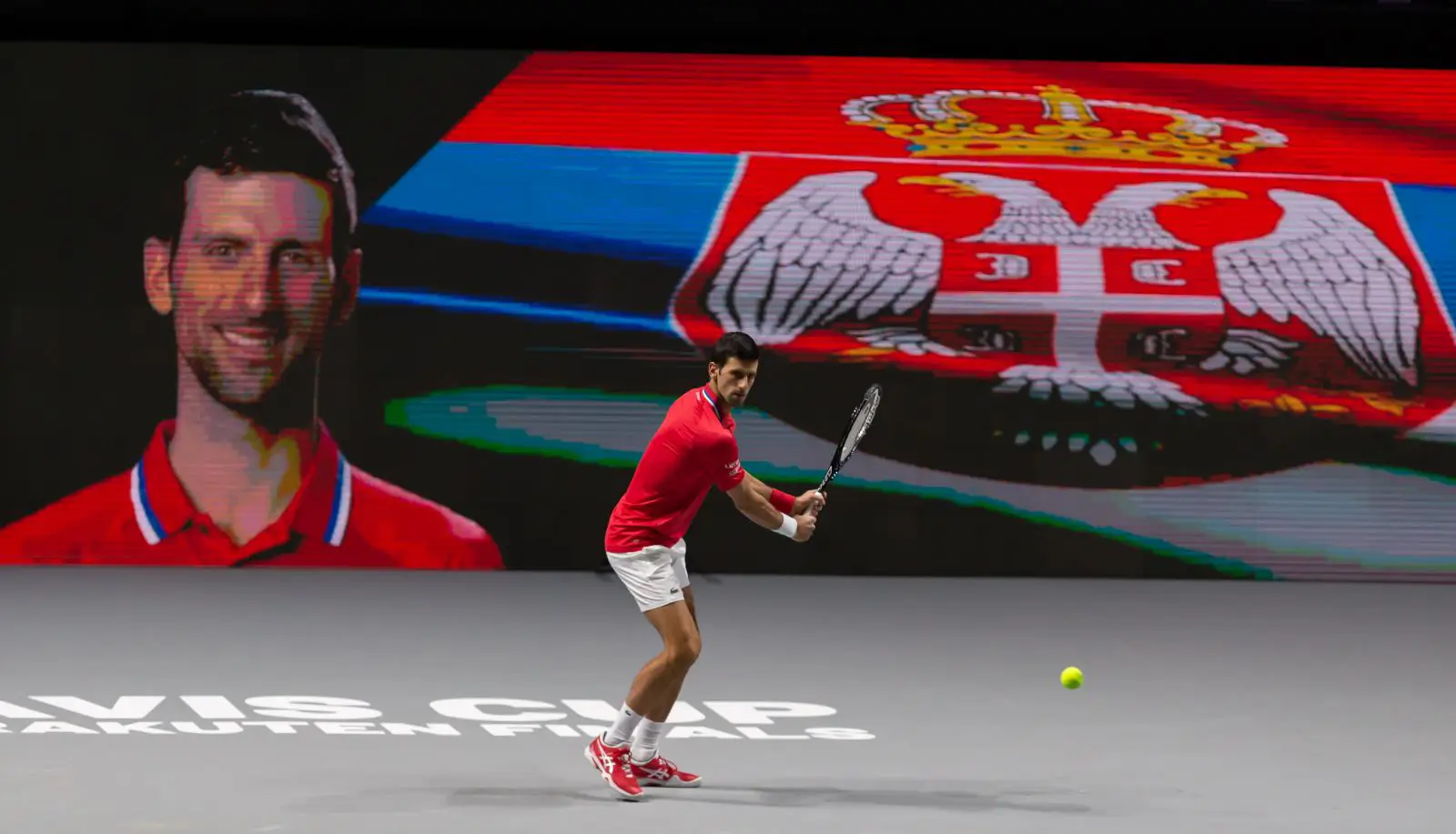 Novak Djokovic playing tennis on indoor court with Serbian flag backdrop