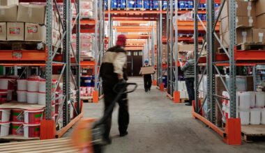 Warehouse interior with workers organizing shelves full of boxes and containers.
