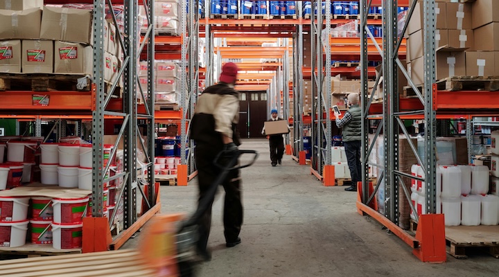Warehouse interior with workers organizing shelves full of boxes and containers.